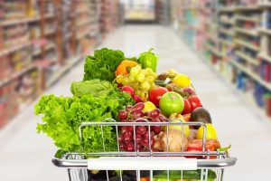 Grocery shopping cart with vegetables and fruits on supermarket background.